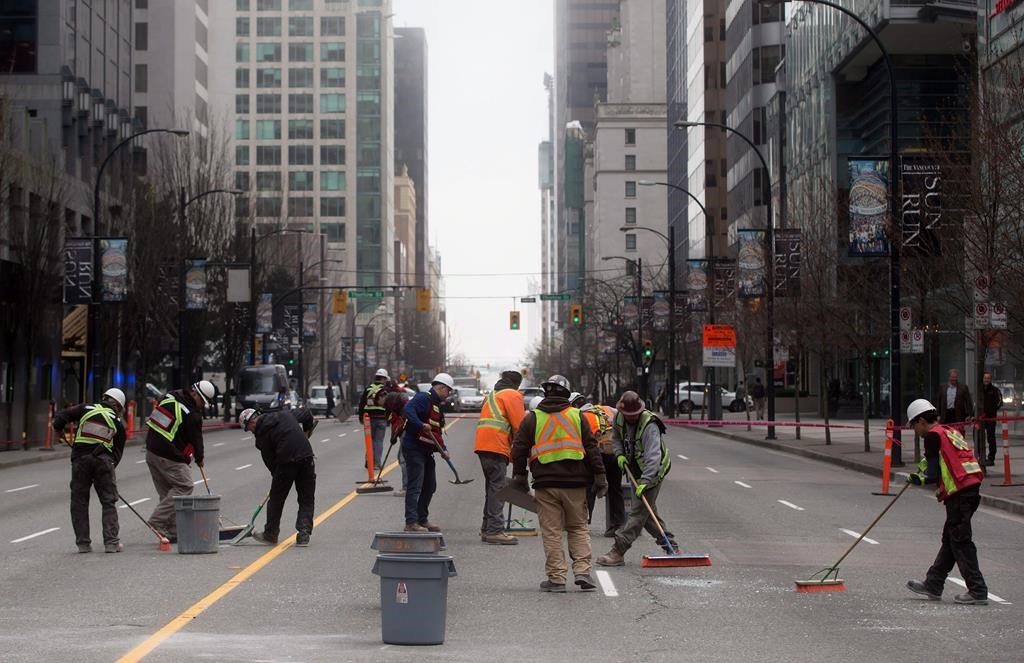 Workers sweep up broken glass after a pane of glass fell from a building under construction in Vancouver, B.C., on March 10, 2015.