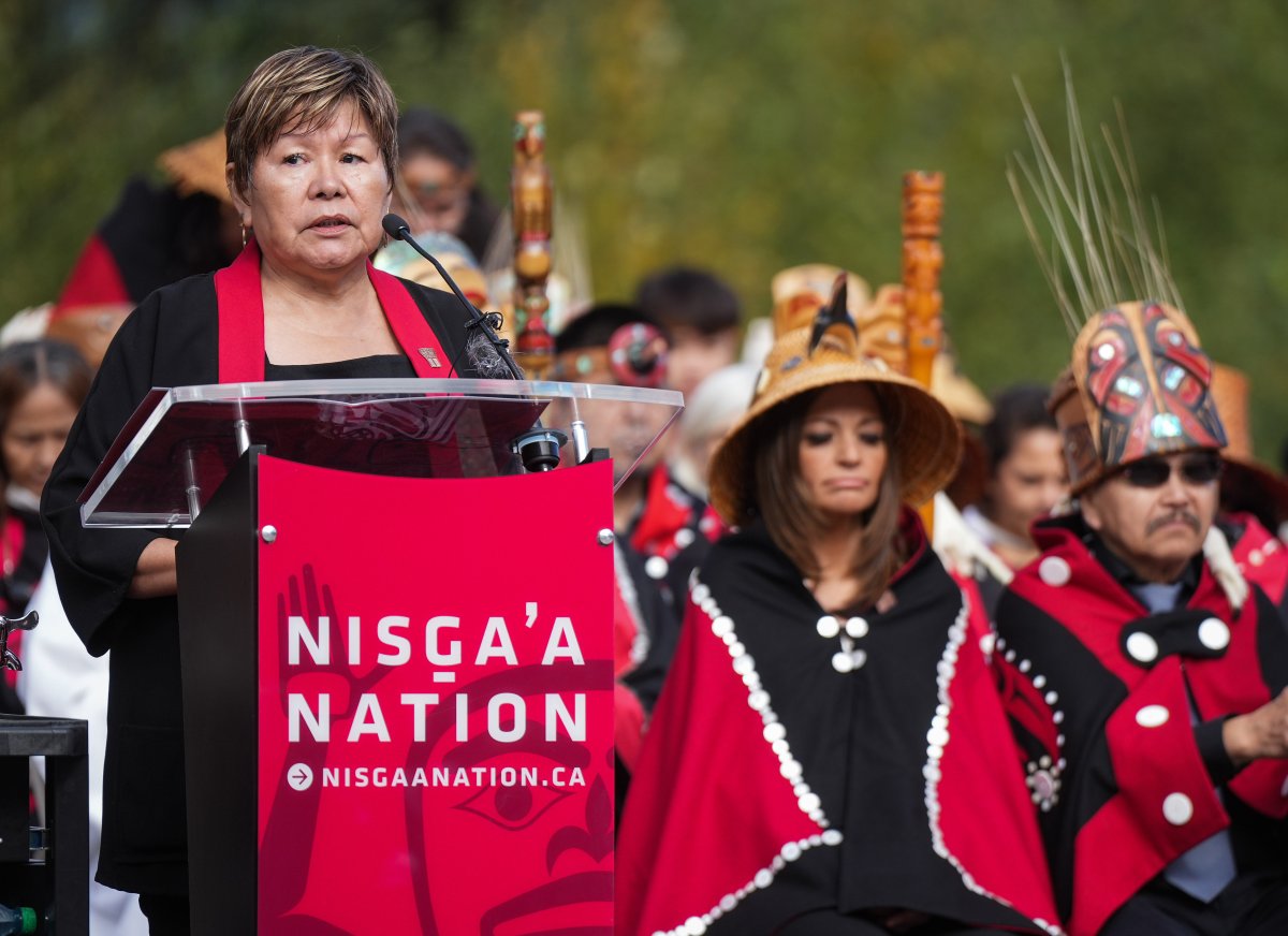 A woman stands behind a podium with people in regalia behind her.