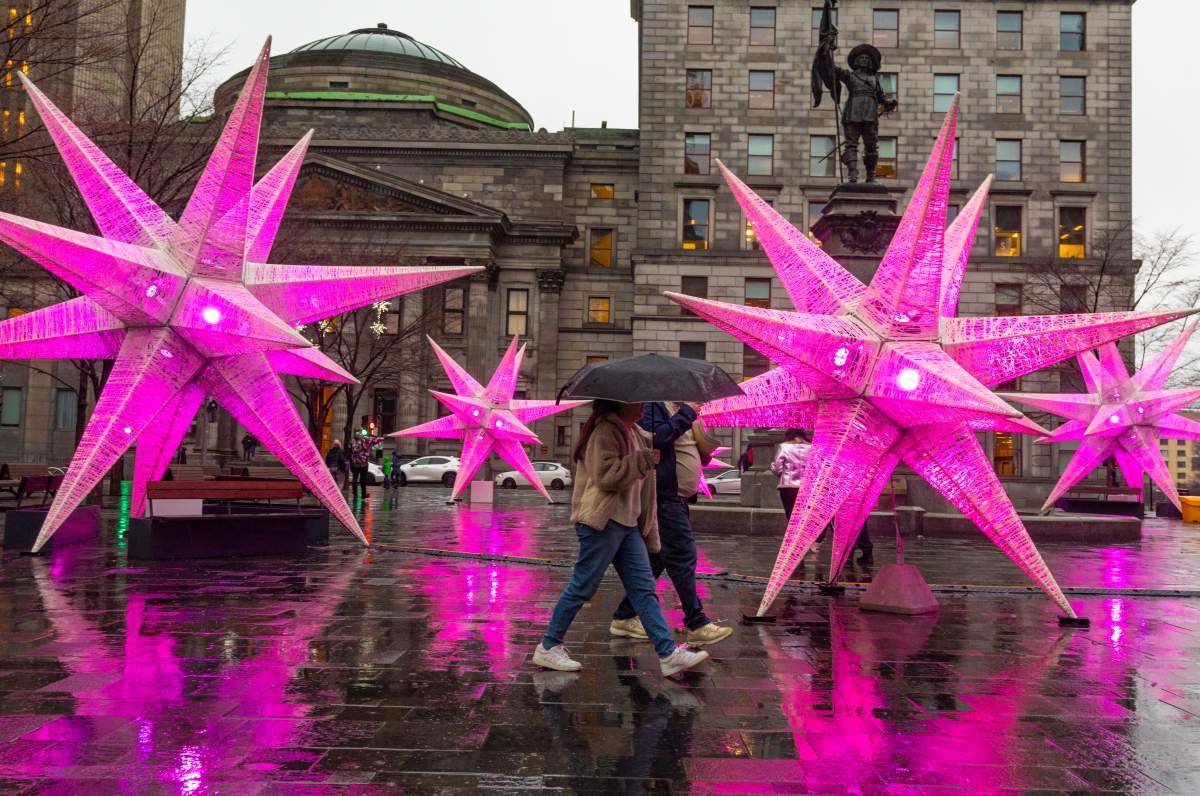 People use umbrellas as they walk past holiday decorations in Montreal’s Place d’Armes. Monday, Dec. 18, 2023.