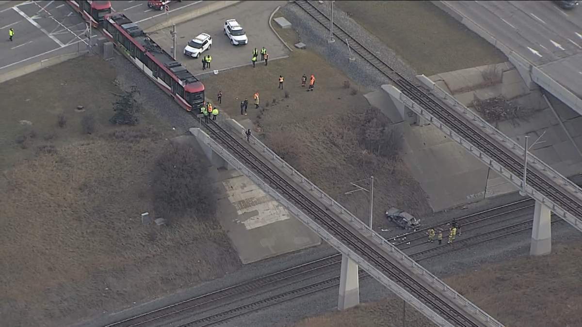 A sedan is seen at the bottom of an embankment, with a CTrain stopped nearby in Calgary midday on Dec. 1, 2023.