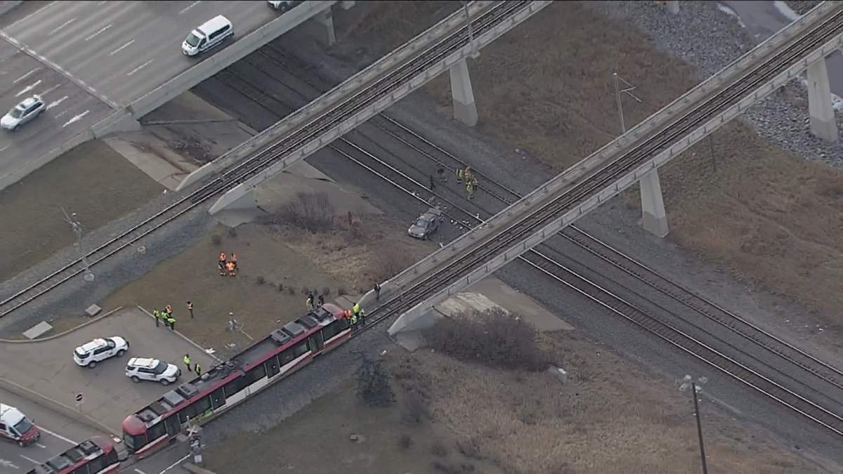 A sedan is seen at the bottom of an embankment, with a CTrain stopped nearby in Calgary midday on Dec. 1, 2023.
