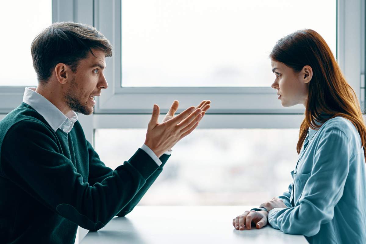 A man and a woman are talking intensely at a table near the window.