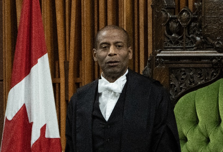 Greg Fergus stands in front of a Canadian flag and the Speaker's chair in the House of Commons