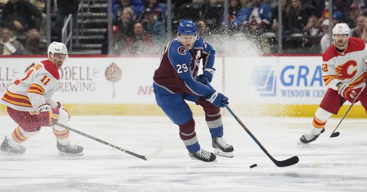 Colorado Avalanche centre Nathan MacKinnon, centre, picks up the puck between Calgary Flames centre Mikael Backlund, left, and defenceman MacKenzie Weegar, right, in the second period of an NHL hockey game Monday, Dec. 11, 2023, in Denver.