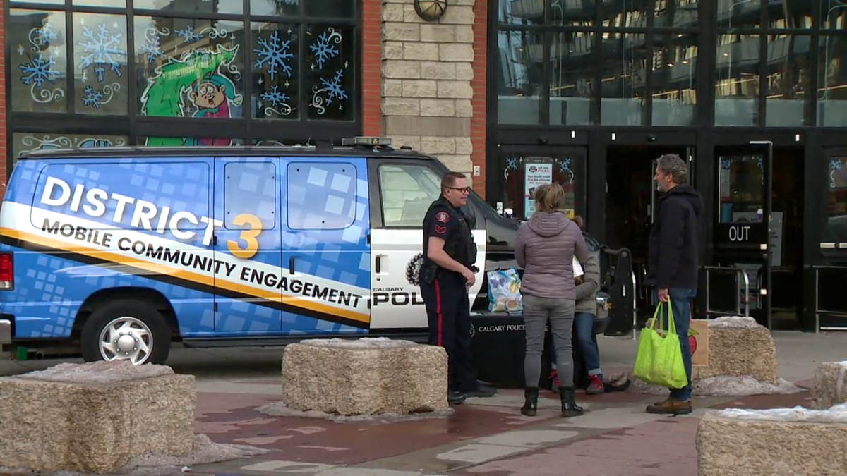 Acting Sgt. Anthony Thompson stands beside the Calgary Police Service community engagement vehicle outside a grocery store, talking with members of the public on Dec. 13, 2023.