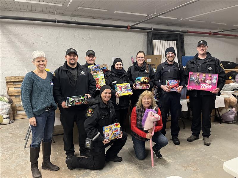 A group of parking enforcement officers pose with Salvation Army volunteers, holding toys donated as part of the Toys for Tickets program.