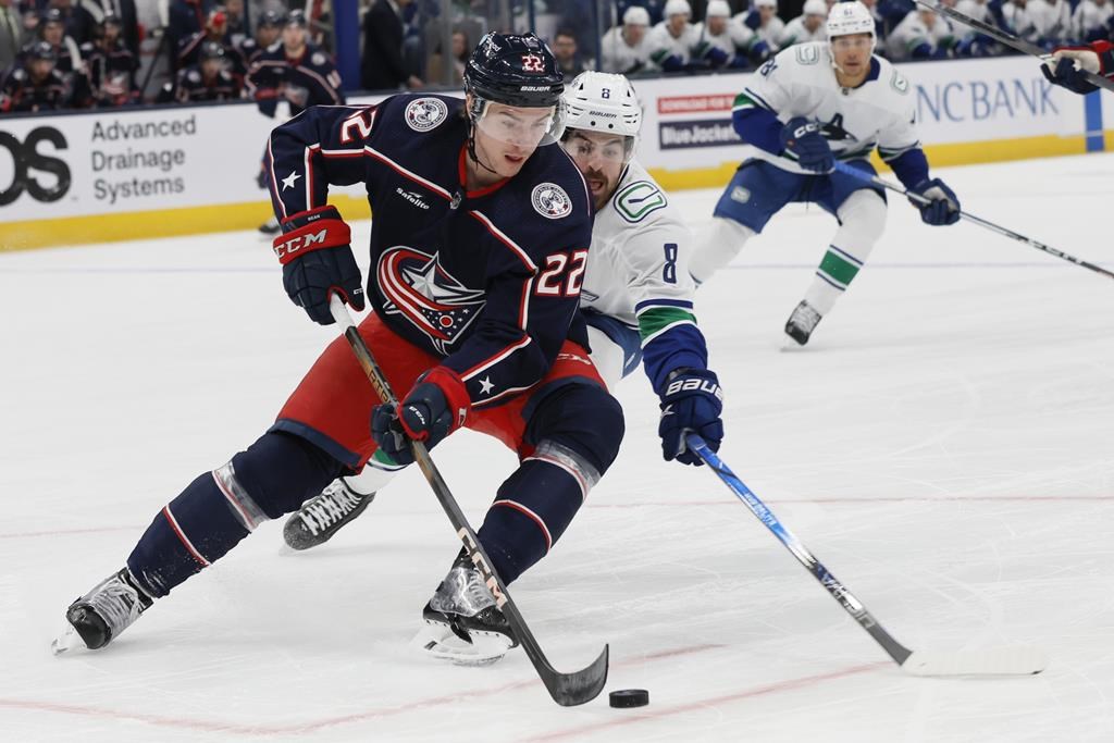 Columbus Blue Jackets' Jake Bean, left, tries to clear the puck as Vancouver Canucks' Conor Garland defends during the first period of an NHL hockey game Monday, Jan. 15, 2024, in Columbus, Ohio.
