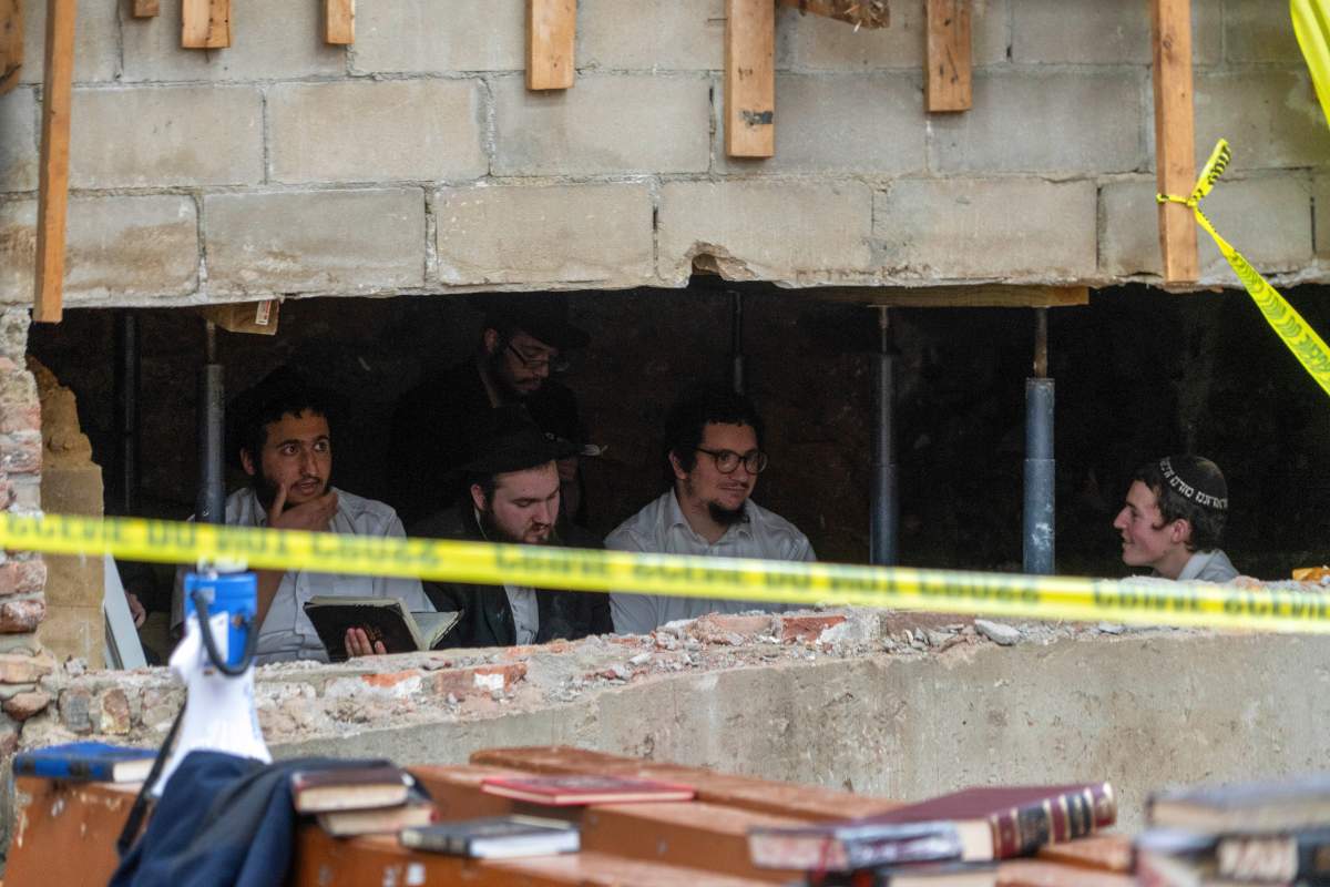 Hasidic Jewish students sit behind a breach in the wall of a synagogue that led to a tunnel dug by the students, Monday, Jan. 8, 2024, in New York.