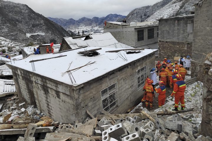 Rescue workers, wearing orange, gather outside a building destroyed in a landslide in China.