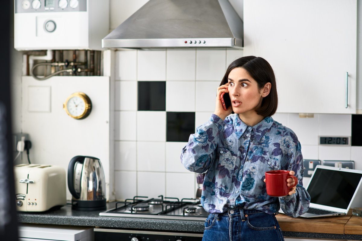 Shocked looking woman on phone in kitchen after finding out Log term disability policy has been removed