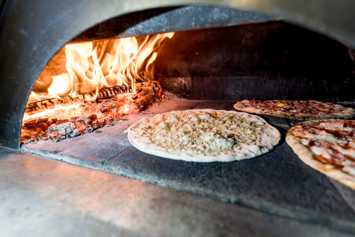 Close-up of three pizzas cooking inside a wood-fired oven.