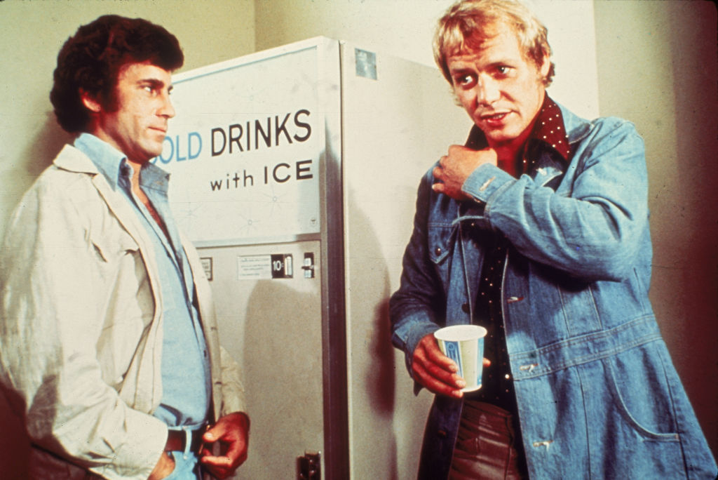 Actors Paul Michael Glaser and David Soul talk by a beverage vending machine in a still from the television series, 'Starsky & Hutch,' 1977.