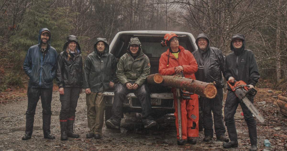 A group of people pose with wood in the back of a pickup truck.