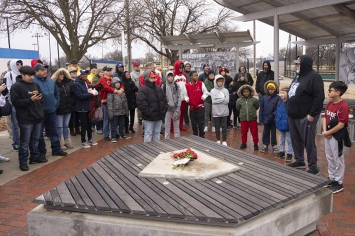 A group of people surround the location where a Jackie Robinson statue was stolen. They are dressed for cold weather.