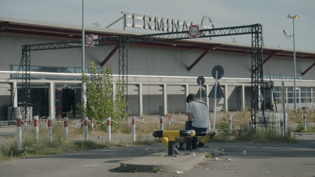 A man sits outside the airport shelter looking at his phone.