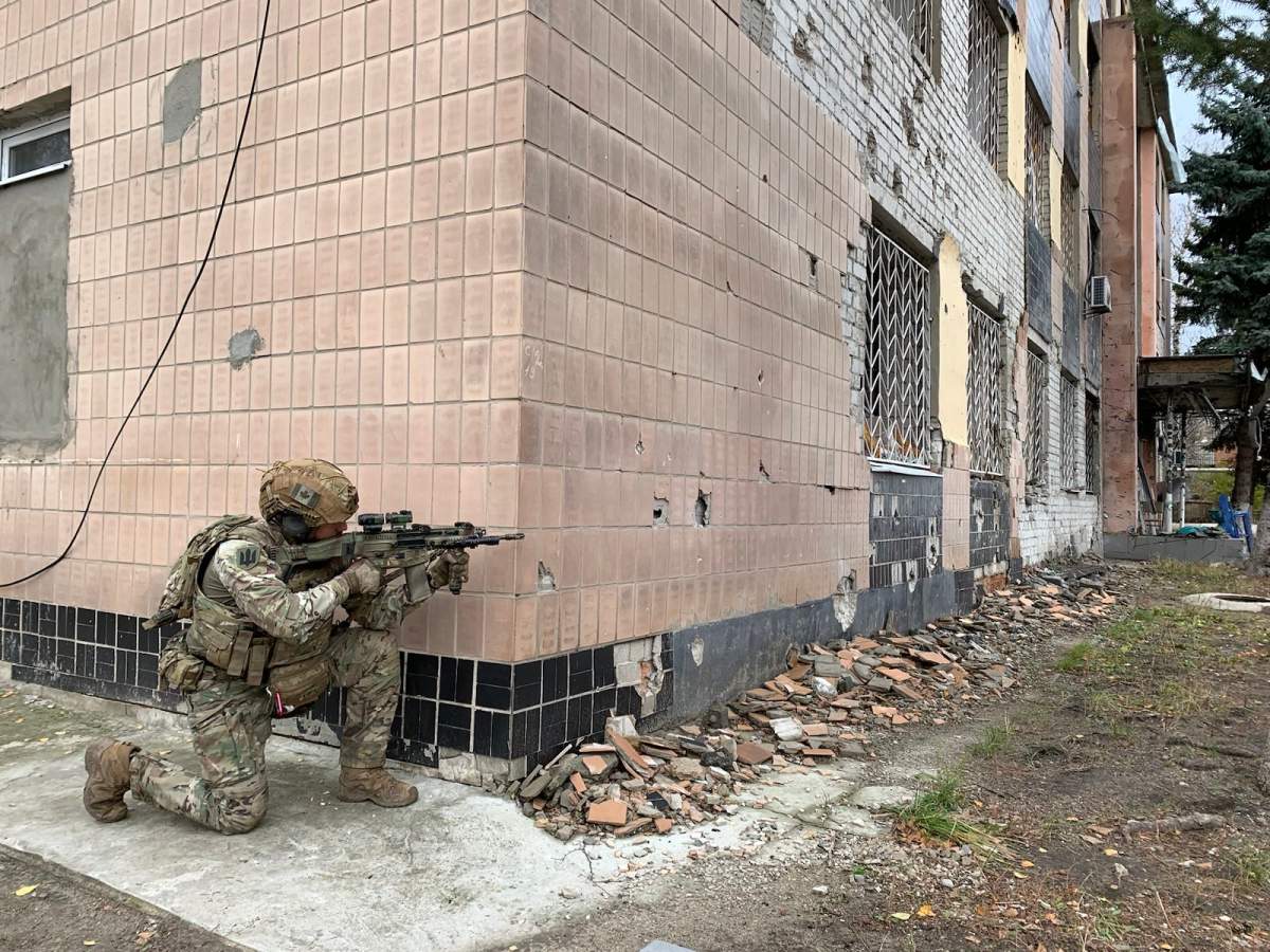 Soldier Dave Smith kneels and aims his rifle at the corner of a damged building in eastern Ukraine
