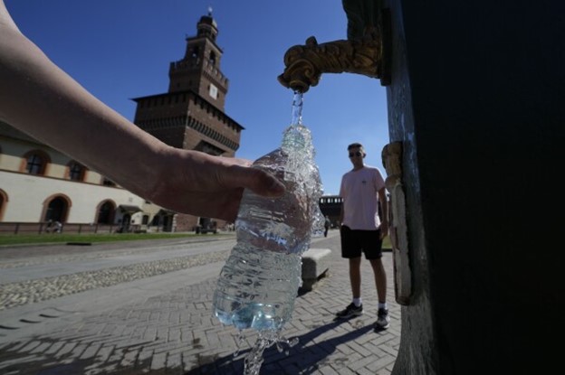 Someone fills an unlabeled plastic water bottle at a public, outdoor tap.