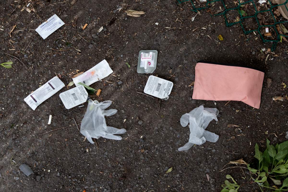 Plastic gloves and the remains of a naloxone drug overdose kit lie on the ground.