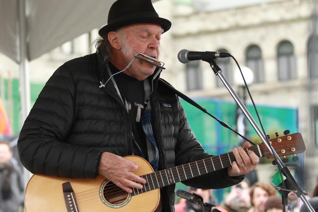 A close-up photo of Neil Young with a guitar outdoors.