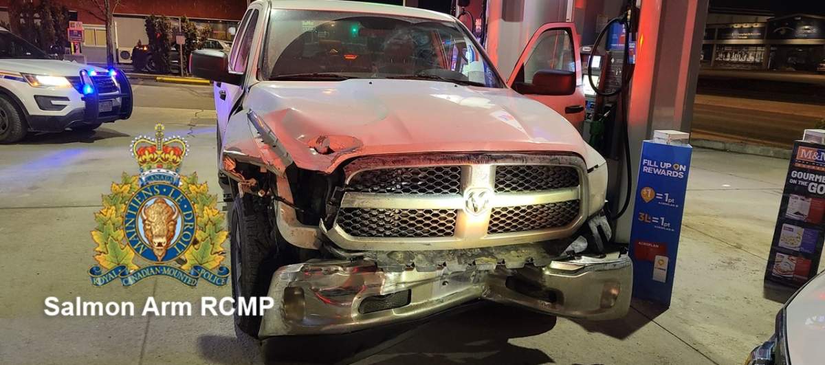 A damaged pick-up truck surrounded by police vehicles at a gas station.
