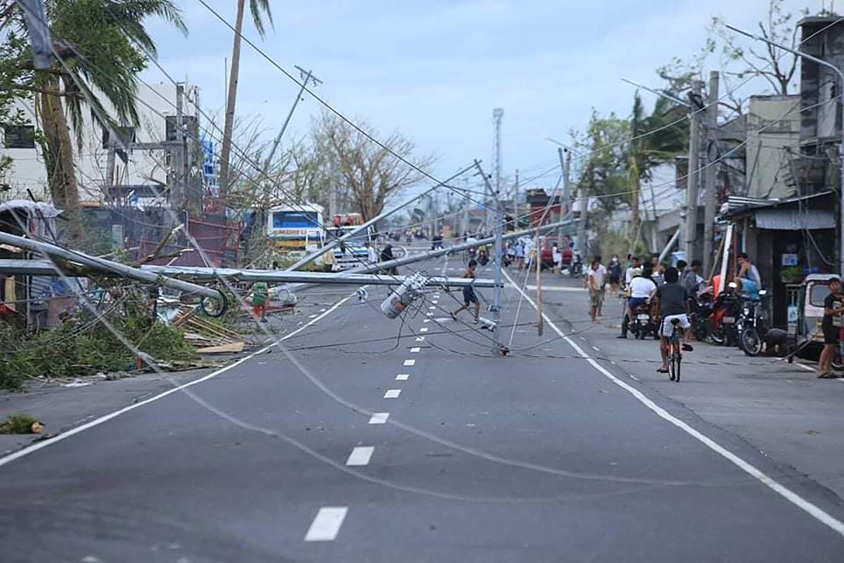 Residents walk next to toppled electric posts destroyed at the height of super Typhoon Goni after it hit Tabaco, Albay province, south of Manila on November 1, 2020.