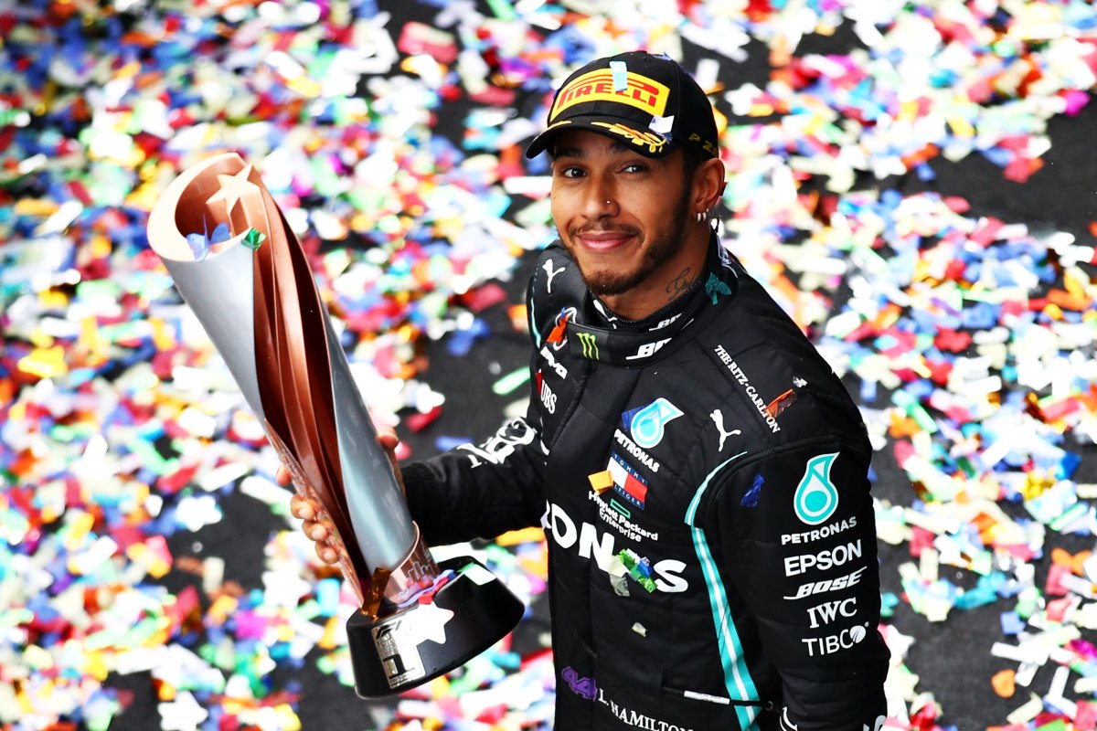 Lewis Hamilton holding an F1 trophy. There is confetti on the ground.