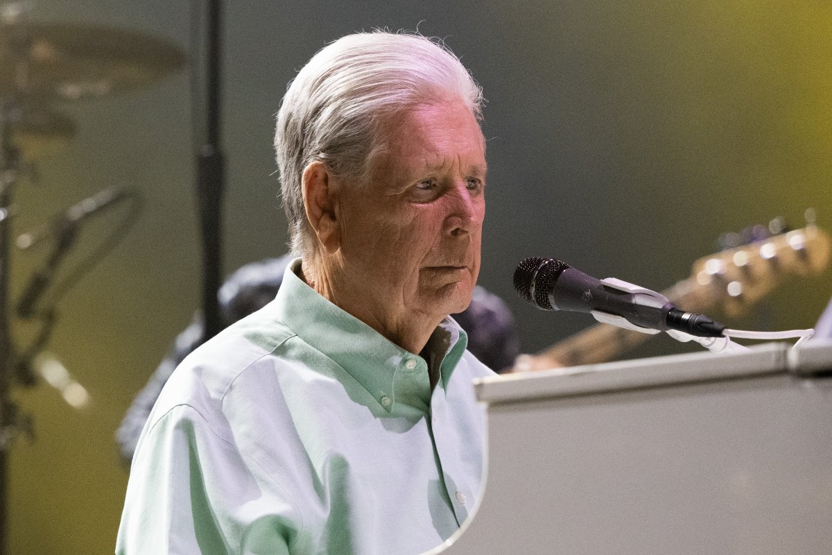 Brian Wilson at a white piano. His wearing a green button up.