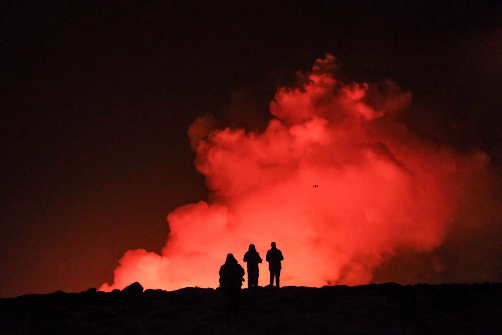A group of people observe molten lava and billowing smoke pouring out of a fissure during a volcanic eruption near Grindavik, western Iceland on February 8, 2024.