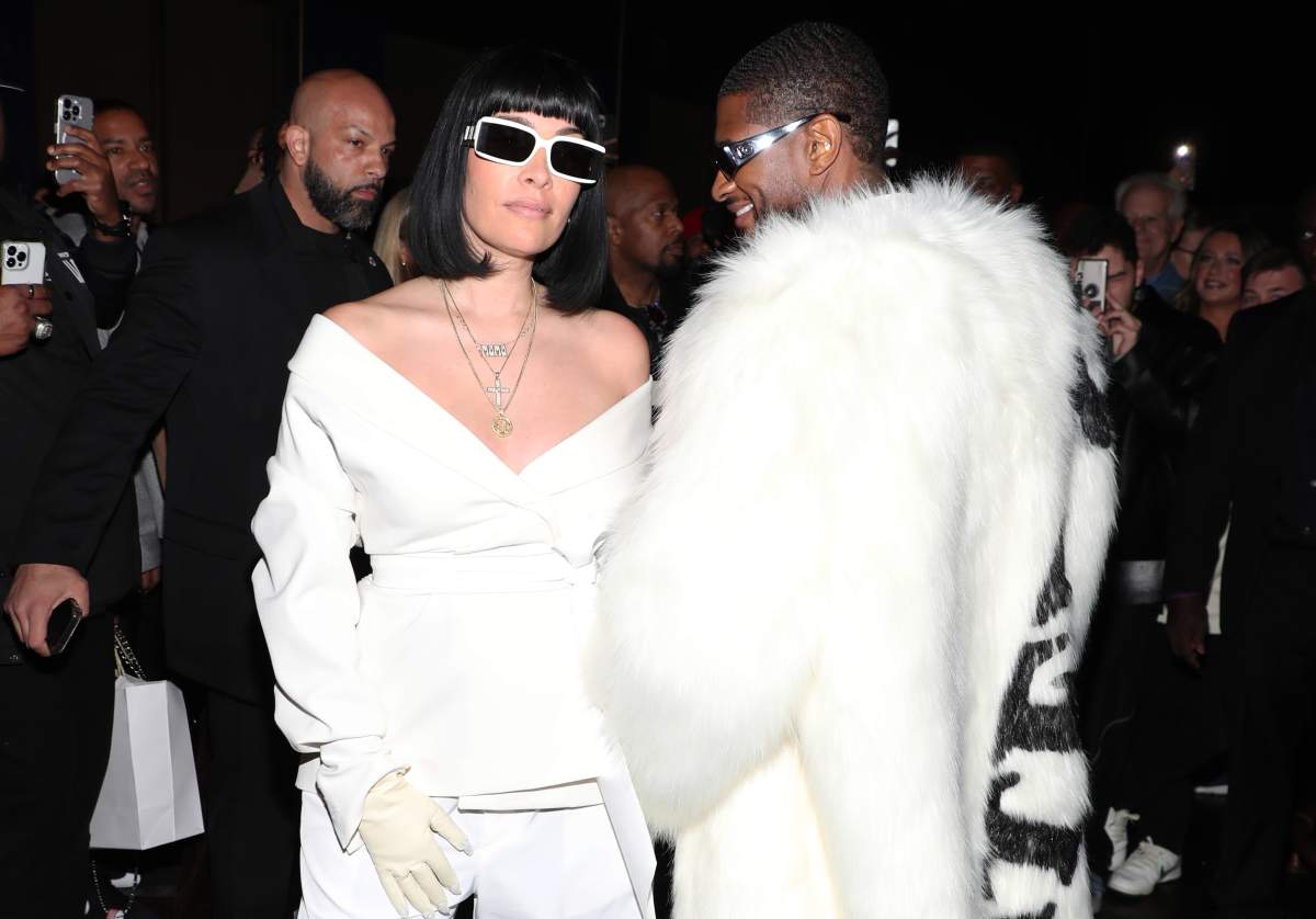 Usher and Jennifer Goicoechea. She is wearing a white pantsuit, white sunglasses and white gloves. Usher has his back half-turned, and is wearing dark sunglasses and a large, white fur coat.