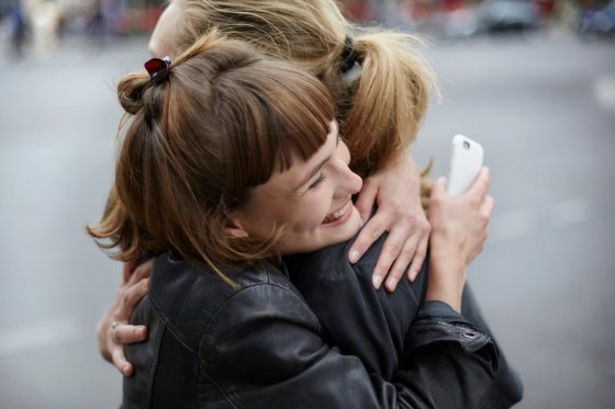 Two female friends with cell phone hugging