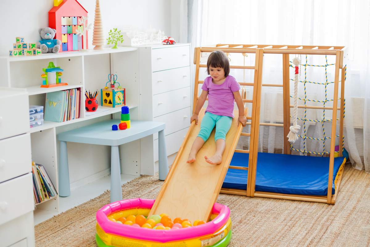 little girl having fun riding a roller coaster on a wooden home sports gaming complex stairs, rings and rope.