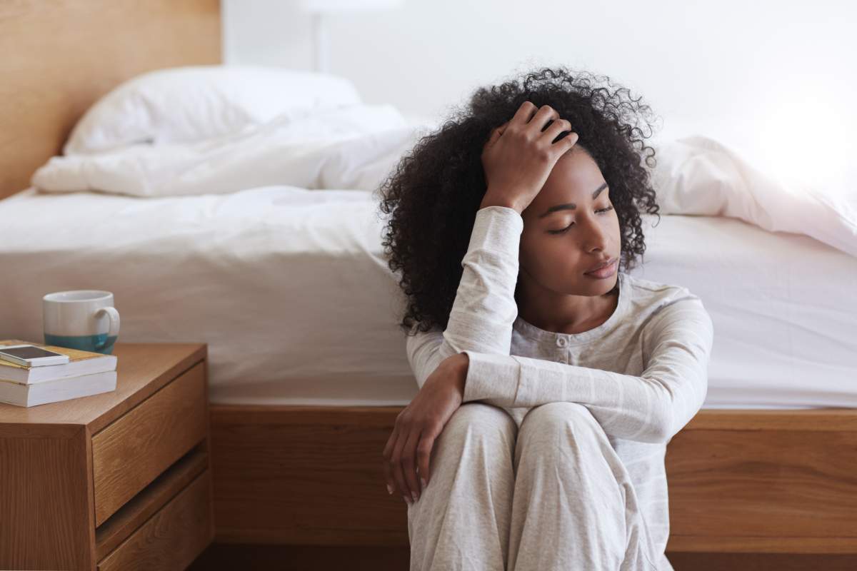 Shot of a tired young woman sitting on the floor leaning against her bed