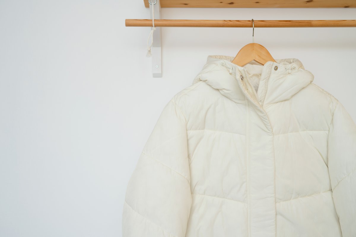 A white jacket with a hood hanging on a wooden hanger.
