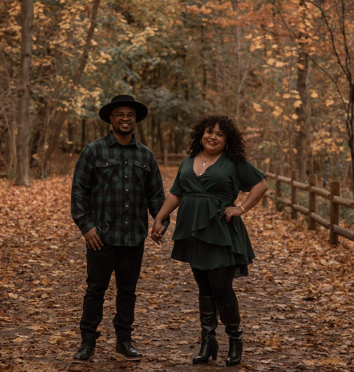 A photo of a couple holding hands outdoors with fall foliage behind them.