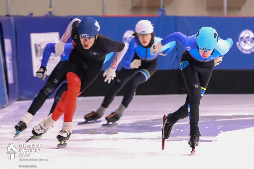 Speed Skaters of the 2024 Alberta Winter Games round the final turn with the finish line ahead.