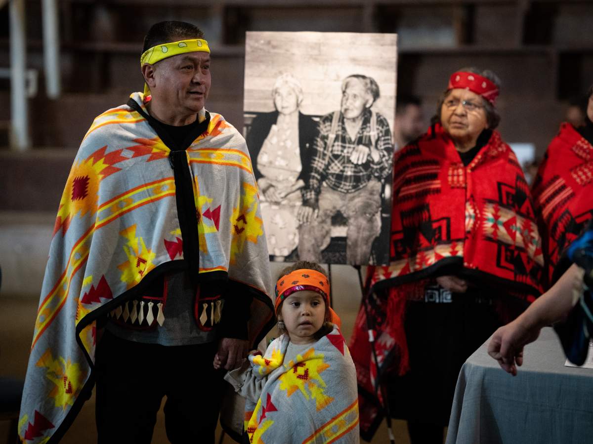 A group of people stand, draped in blankets in front of an archive photo.