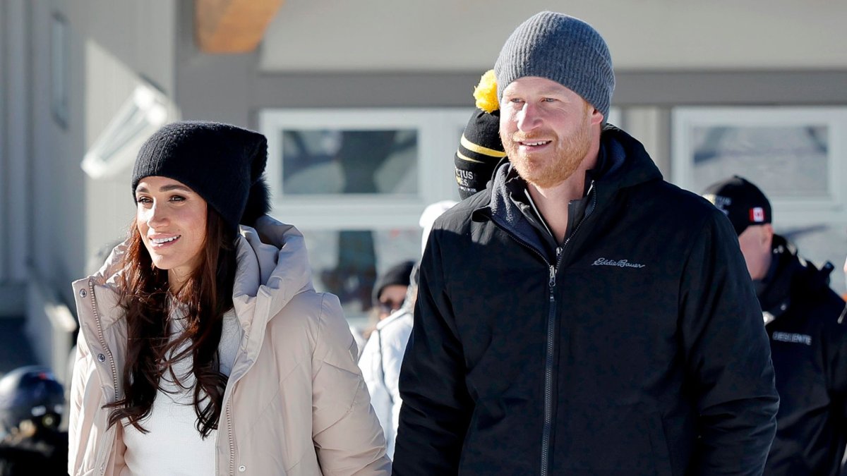 Meghan Markle and Prince Harry on a snowy hill. Meghan Markle is wearing a black toque and cream coat. Harry is wearing a black coat and a grey toque,
