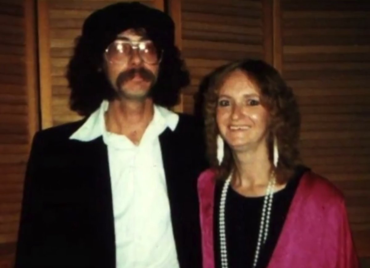 A photograph of a man with large glasses and a mustache and a woman in a pink blazer.
