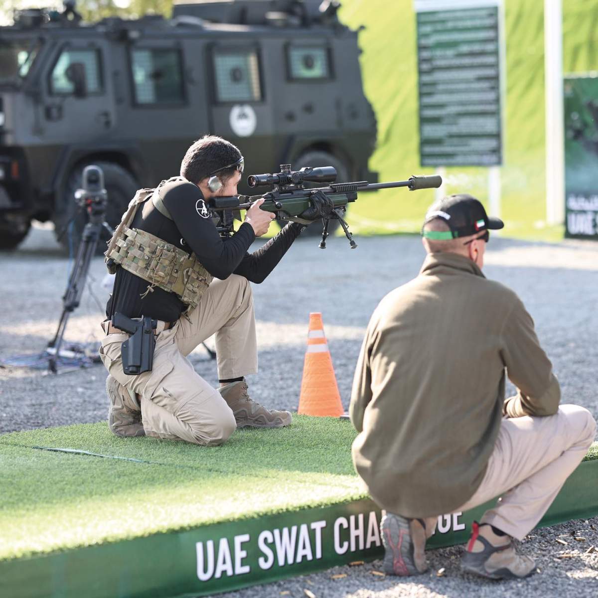 Someone on a platform with a firearm and a tactical vehicle in the background.