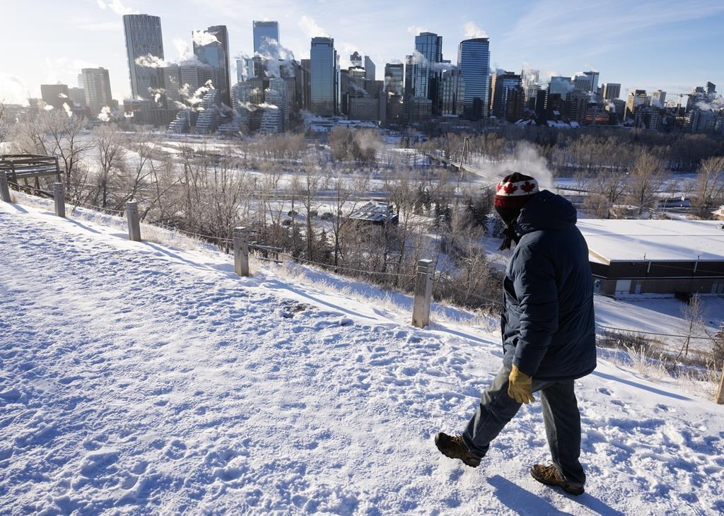 A man walks by the city skyline in Calgary, Alta.
