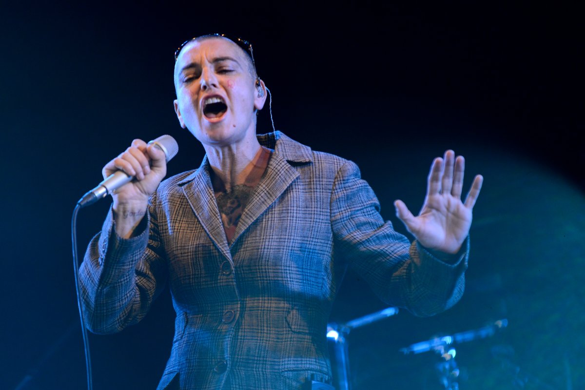 Sinéad O’Connor singing on stage, She is wearing a tweed jacket and her head is shaved.