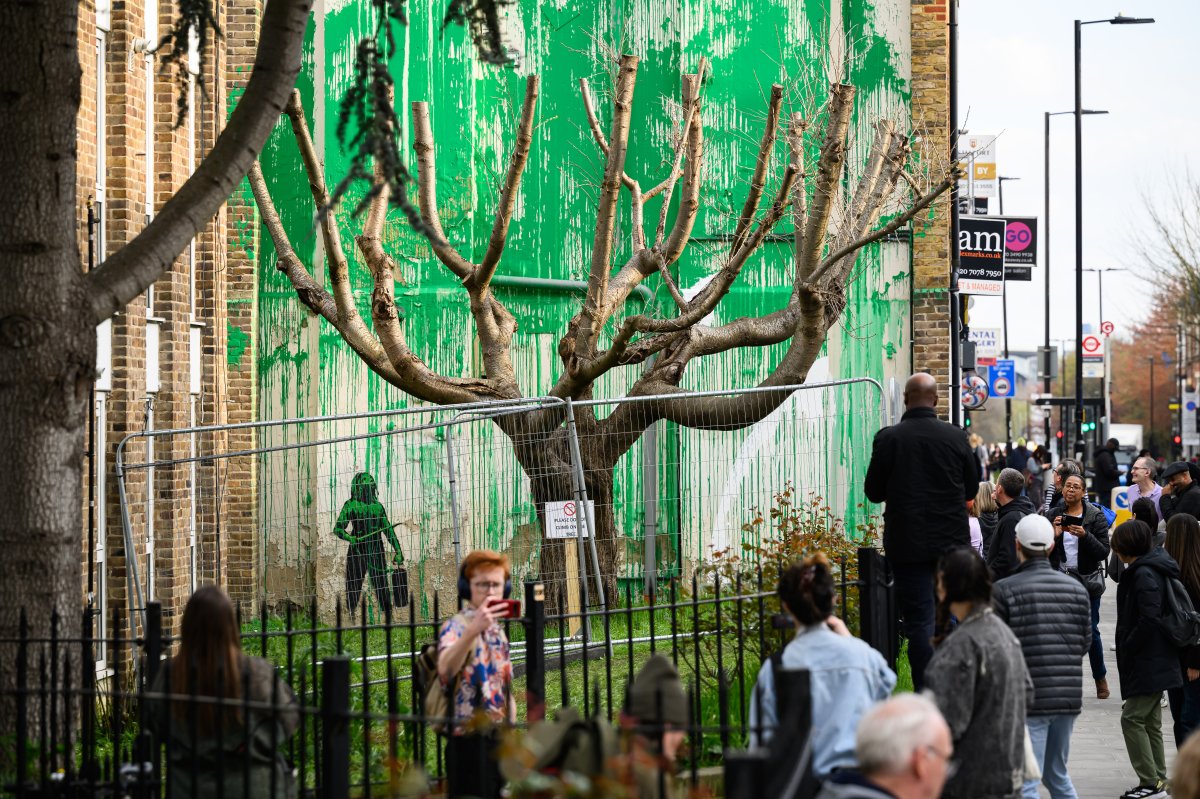 Members of the public look at a mural by the artist Banksy following it's defacement with white paint, on March 20, 2024 in the Finsbury Park area of London, England.