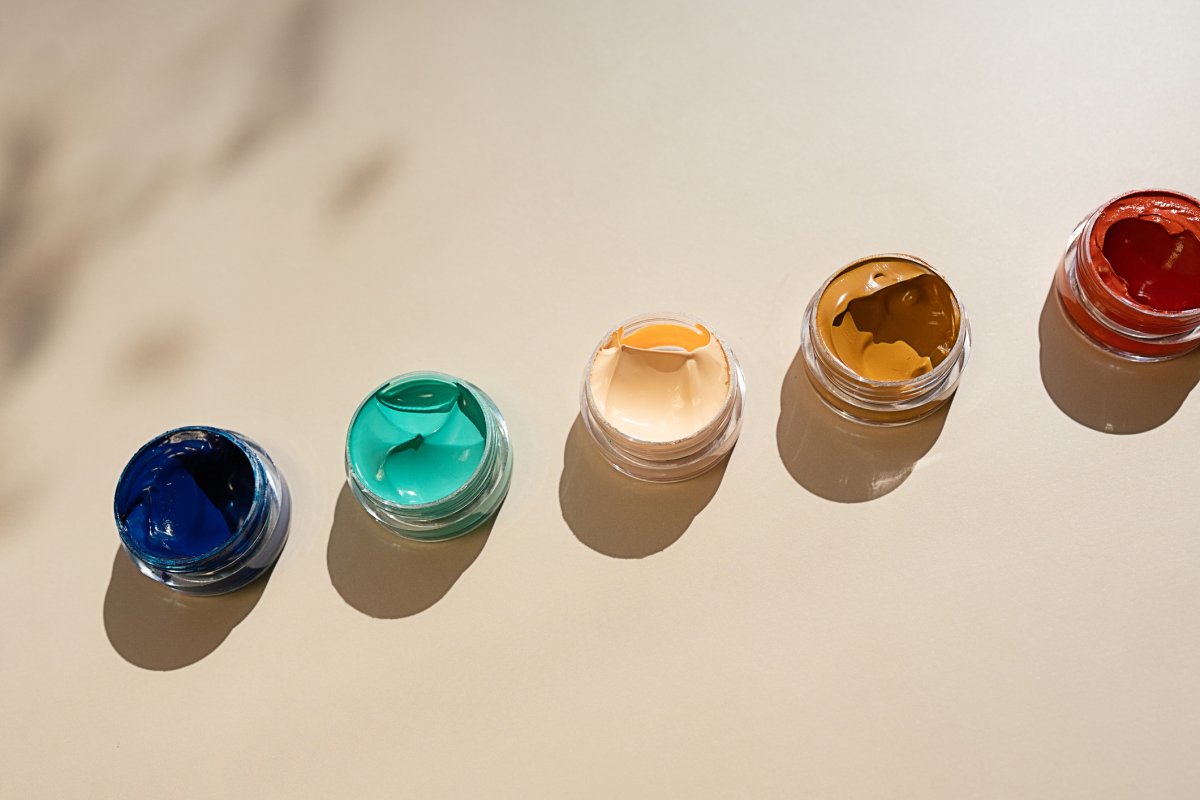 Array of open paint jars in a gradient of colors on a neutral background with playful shadows