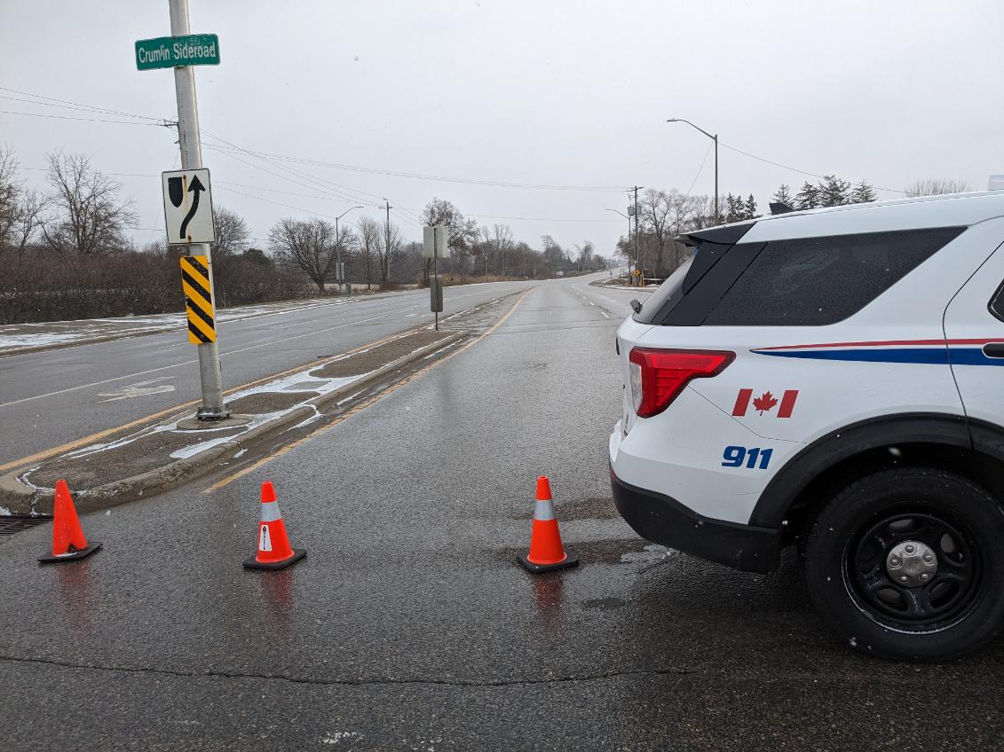 A police cruiser and pylons blocking a road on a cold winter day.