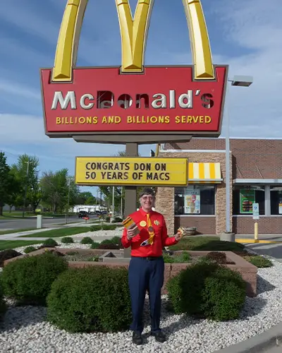 Donald Gorske in front of a McDonald's sign missing the letters D, O, N and S. The menu board below reads, 