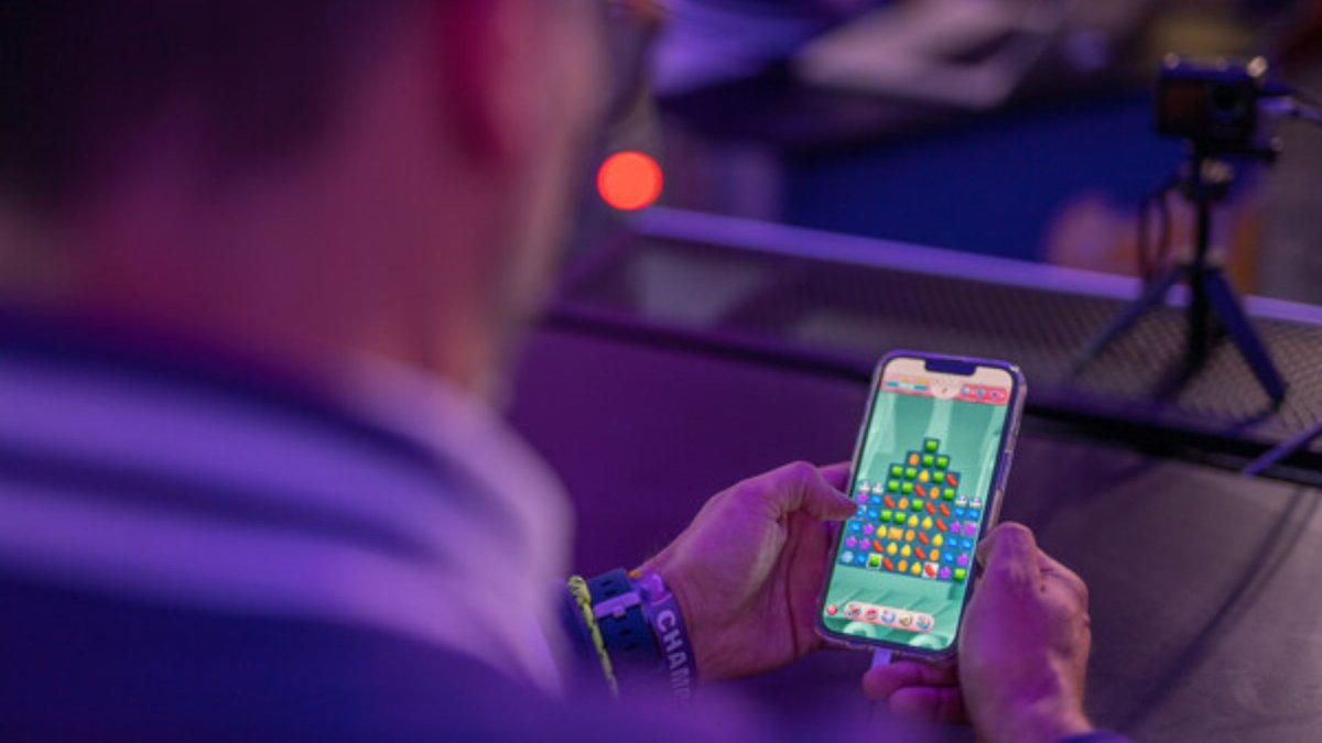 A man with glasses, photographed from behind is playing Candy Crush Saga.