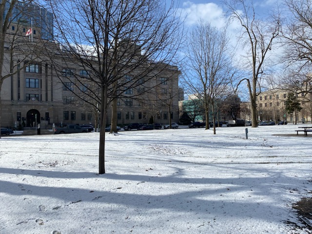 Snow on the ground in front of a large building on a sunny day.