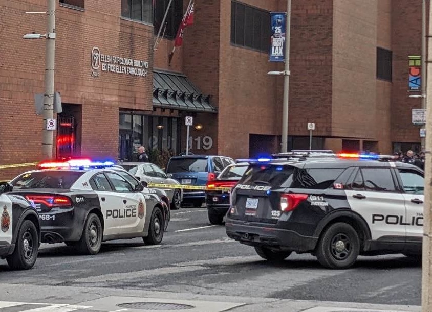 Hamilton police cruisers and caution tape outside of a red brick building.