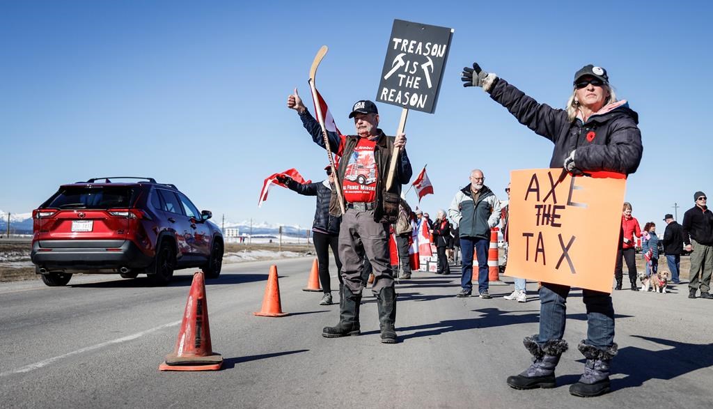 Anti-carbon levy protesters wave signs and chant slogans as they block a westbound lane of the Trans-Canada highway near Cochrane, Alta., Monday, April 1, 2024.THE CANADIAN PRESS/Jeff McIntosh