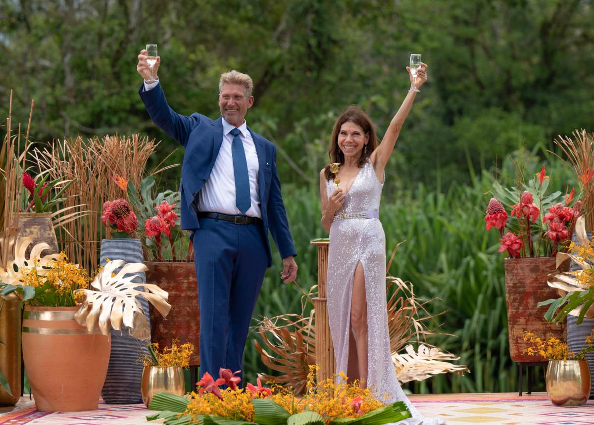 Gerry Turner and Theresa Nist in a tropical place, wearing formalwear. They are holding champagne flutes.